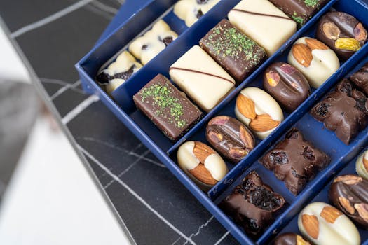 Assortiment de chocolats fins avec praliné, amandes et pistaches dans une boîte bleue élégante.