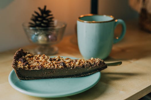Une part de tarte au chocolat sur une assiette bleue, garnie de noix, avec une tasse turquoise en arrière-plan.