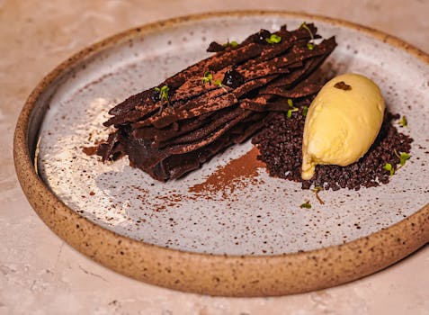 Tarte au chocolat avec ganache montée, sablé fleur de sel, meringue cacao et boule de glace sur assiette élégante.