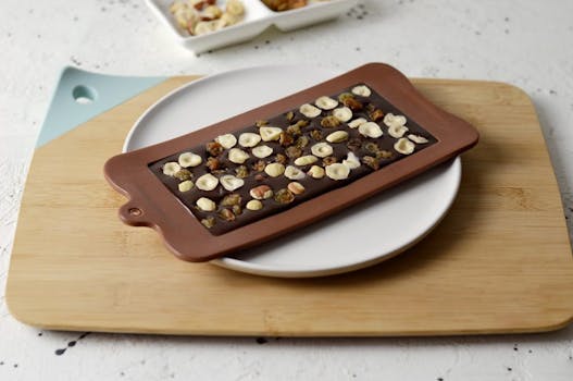 Tablette de chocolat praliné avec des noisettes sur une assiette blanche, posée sur une planche en bois.